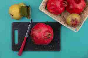 Free photo top view of fresh pomegranate on a black kitchen board with knife with a bucket of fruits on a blue background