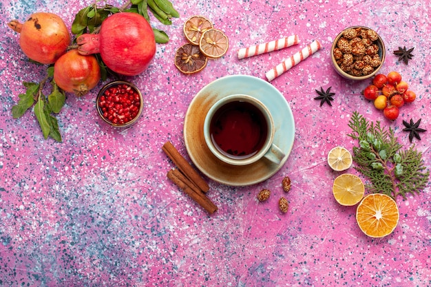 Бесплатное фото Вид сверху свежего граната с зелеными листьями и чашкой чая на светло-розовой поверхности