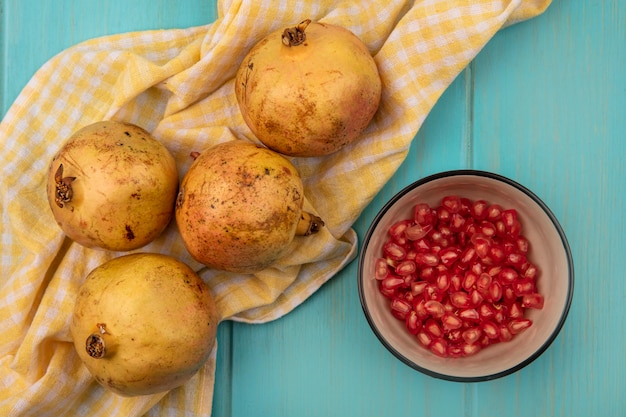 Free photo top view of fresh pomegranates isolated on a yellow checked cloth with pomegranate seeds on a bowl on a blue wooden wall