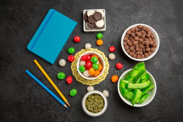 Top view fresh pumpkin seeds with cookies and colorful candies on dark-grey background rainbow color seed candy