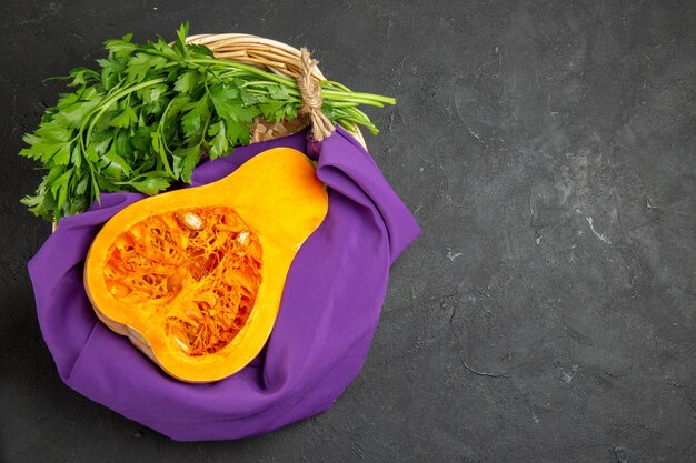 Top view of fresh pumpkin with greens inside basket on dark desk