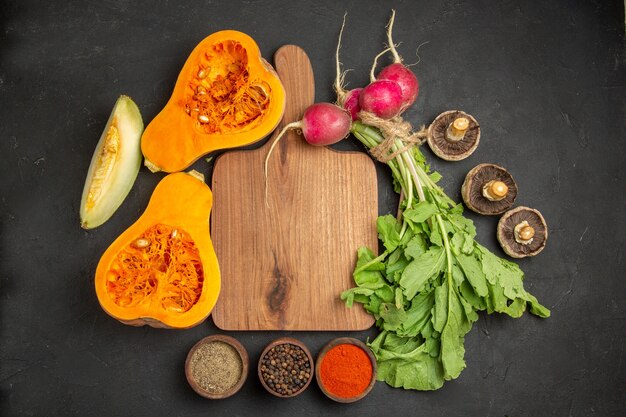 Top view of fresh pumpkin with greens and radish on a dark background