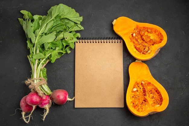 Top view of fresh pumpkin with greens and radish on dark background