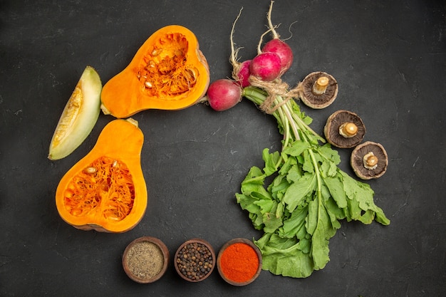 Top view of fresh pumpkin with greens and radish on dark desk