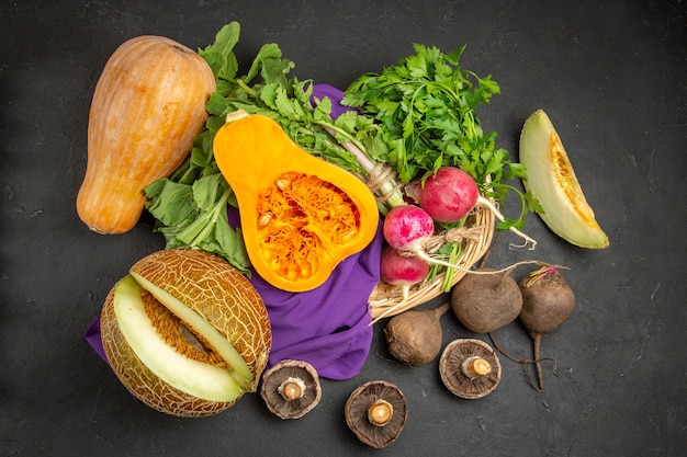 Top view of fresh pumpkin with melon radish and greens on dark background