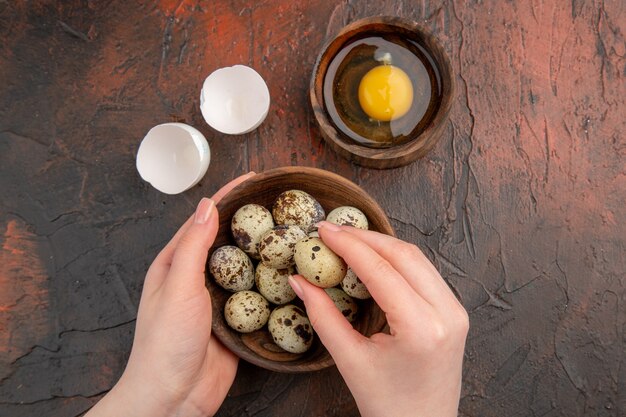 Top view fresh quail eggs with raw egg inside plate on dark table