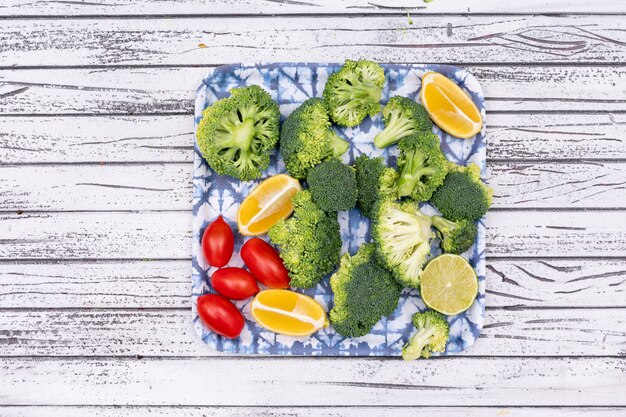 Top view fresh raw broccoli sliced lemon cherry tomatoes in plate on wooden surface