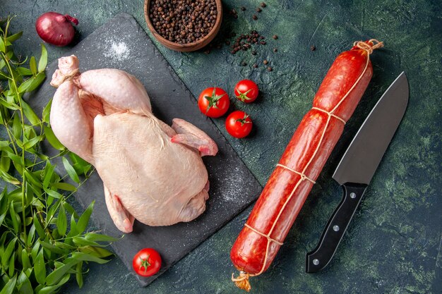 Foto gratuita vista dall'alto pollo crudo fresco con pomodori rossi e salsiccia su sfondo scuro pasto foto animale colore alimentare pollo carne da cucina