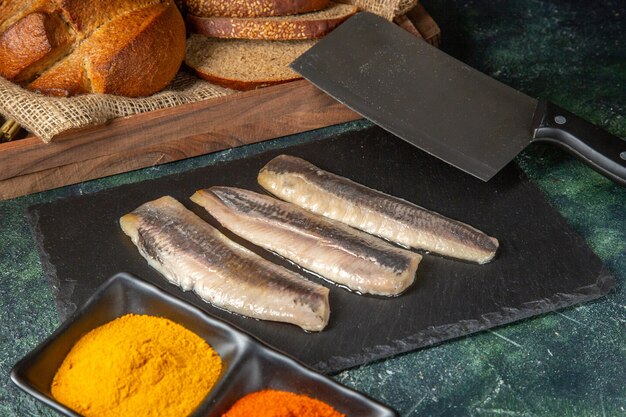 Вид сверху свежей сырой нарезанной рыбы на черной деревянной разделочной доске, специи, хлебный тесак
