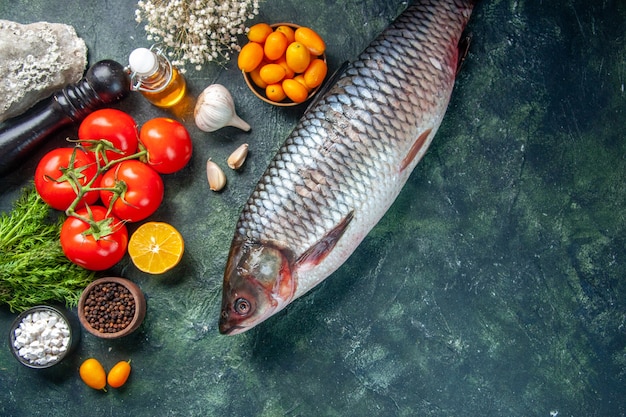 Vista dall'alto pesce crudo fresco con kumquat e pomodori su sfondo scuro