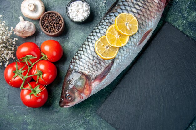 top view fresh raw fish with lemon slices and tomatoes on dark blue background