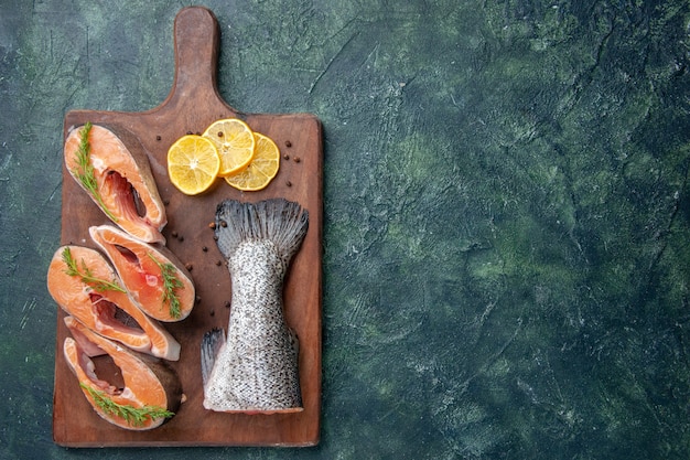 Foto gratuita vista dall'alto di pesce crudo fresco fette di limone verdi pepe sul tagliere di legno sul lato destro sul tavolo colori mix scuri