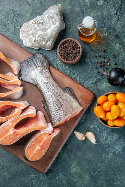 Top view of fresh raw fishes on wooden cutting board and oil bottle lemon kumquats garlic on dark mix colors table