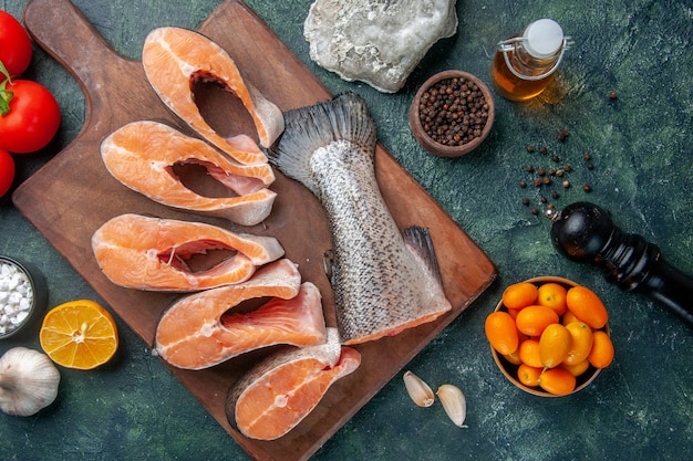 木製のまな板とスパイスオイルボトルレモンキンカンニンニクのダークミックスカラーテーブルの新鮮な生の魚の上面図