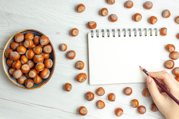 Free photo top view fresh raw hazelnuts with notepad on white table