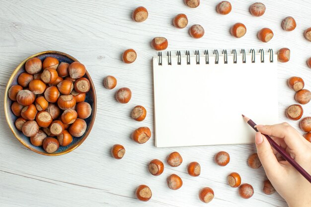 白いテーブルの上のメモ帳で新鮮な生のヘーゼルナッツの上面図