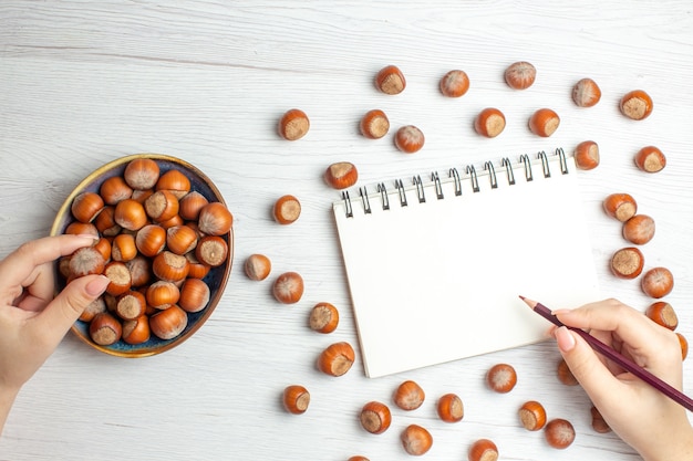 Top view fresh raw hazelnuts with notepad on white table