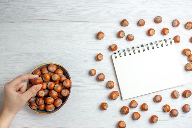 Top view fresh raw hazelnuts with notepad on white table