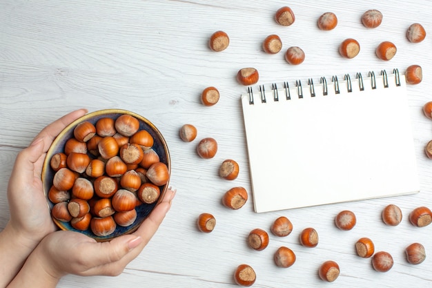 Top view fresh raw hazelnuts with notepad on white table