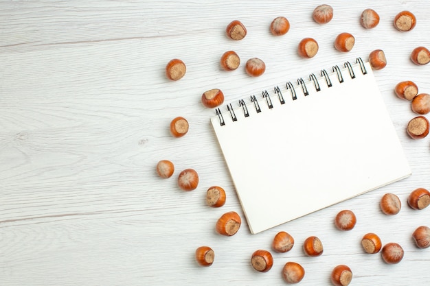 Top view fresh raw hazelnuts with notepad on white table