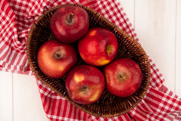 Top view of fresh red apples on a bucket on a red checked cloth on a white wooden wall