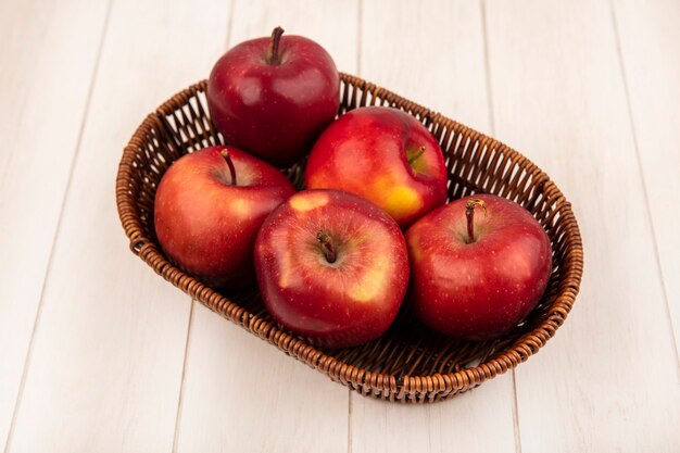 Top view of fresh red apples on a bucket on a white wooden wall