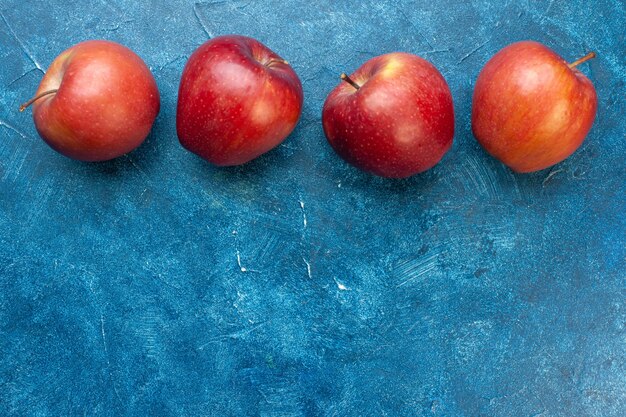 Вид сверху свежие красные яблоки, выложенные на синем столе