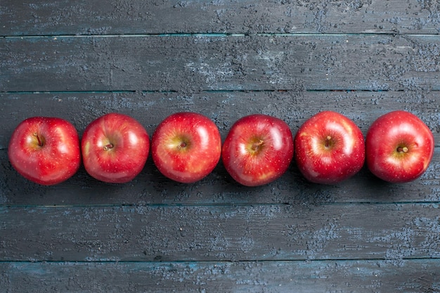 Foto gratuita vista dall'alto mele rosse fresche frutti maturi e morbidi allineati sulla scrivania blu scuro molti frutti di colore rosso albero pianta fresca