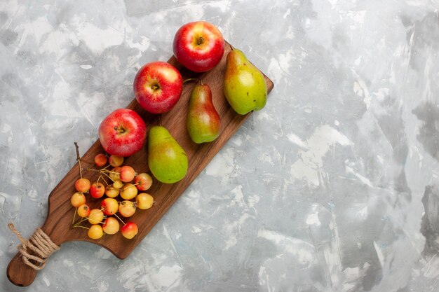 明るい白い机の上に甘いサクランボと梨と新鮮な赤いリンゴの上面図。