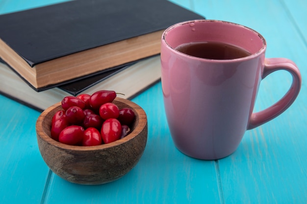 Top view of fresh red cornel berries on a wooden bowl with a cup of tea on a blue wooden background