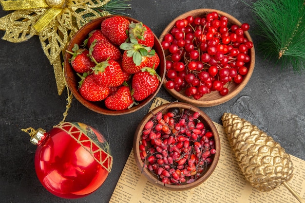 Top view fresh red cranberries with other fruits around christmas toys on a dark background