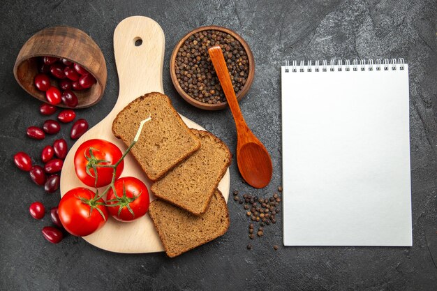 Top view of fresh red dogwoods with bread loafs and tomatoes on grey surface