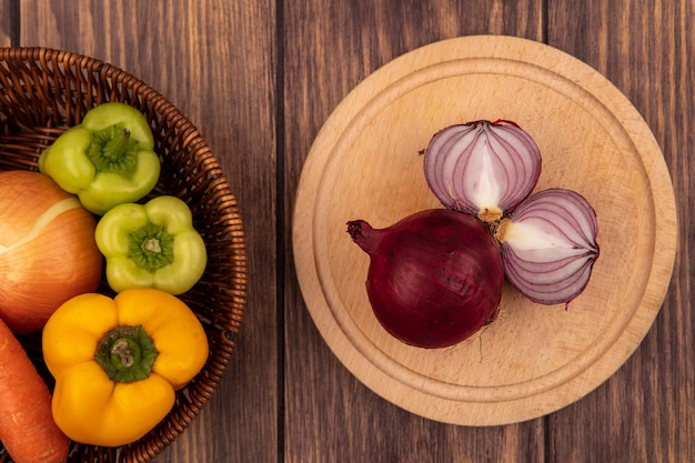 Top view of fresh red onions on a wooden kitchen board with bell peppers and white onion on a bucket on a wooden wall