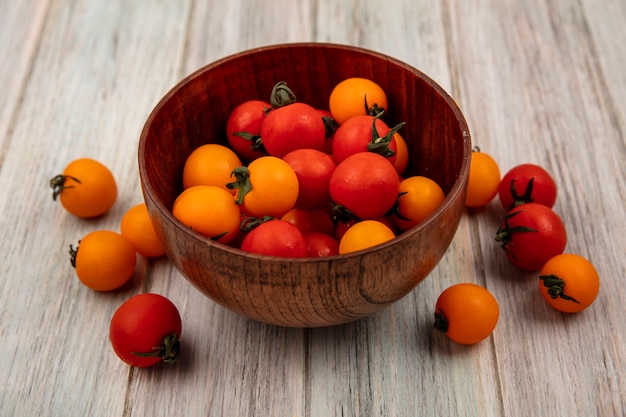 Top view of fresh red and orange tomatoes on a wooden bowl on a grey wooden wall