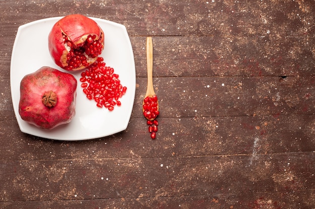 Top view fresh red pomegranates inside plate on a brown rustic desk