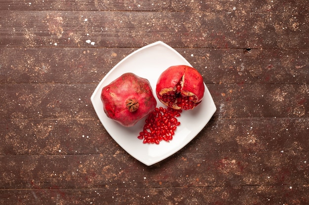 Top view fresh red pomegranates inside plate on brown rustic desk