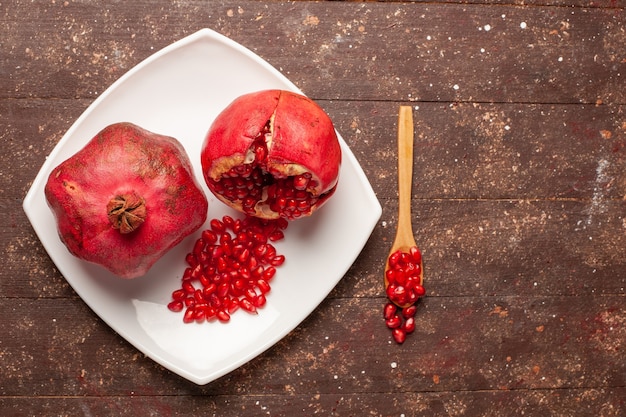 Top view fresh red pomegranates inside plate on the brown rustic desk