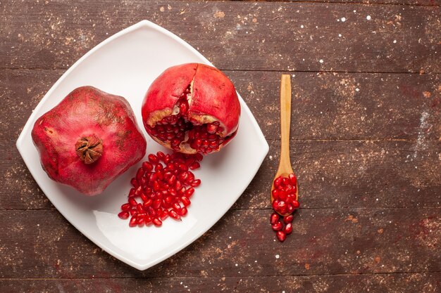 Top view fresh red pomegranates inside plate on the brown rustic desk