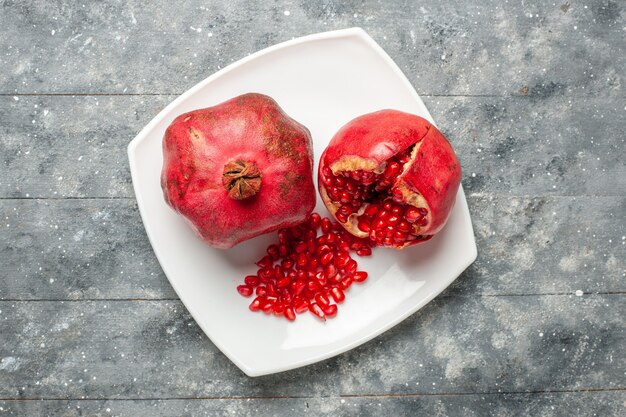 Top view fresh red pomegranates inside plate on grey rustic desk