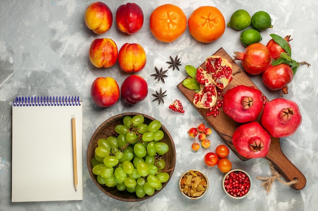 Вид сверху свежие красные гранаты, кислые и спелые фрукты со свежим зеленым виноградом на светло-белом столе