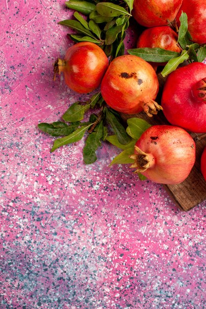 Top view fresh red pomegranates with green leaves on pink desk