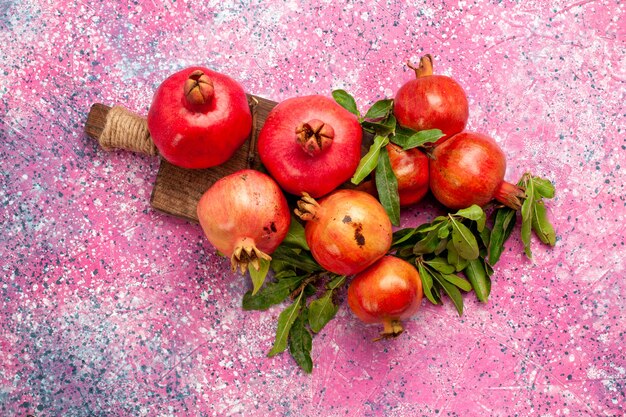 Top view fresh red pomegranates with green leaves on pink surface