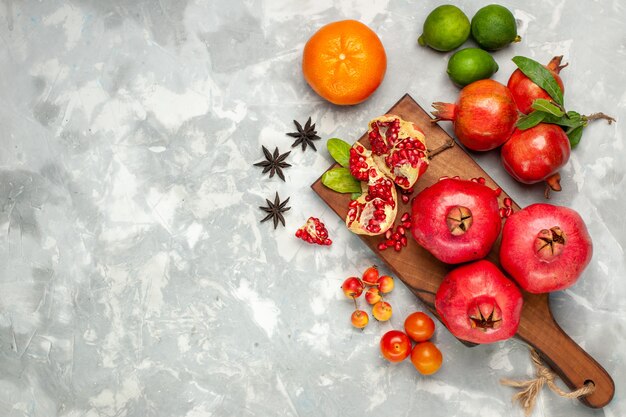 Free photo top view fresh red pomegranates with tangerines and plums on the light-white desk