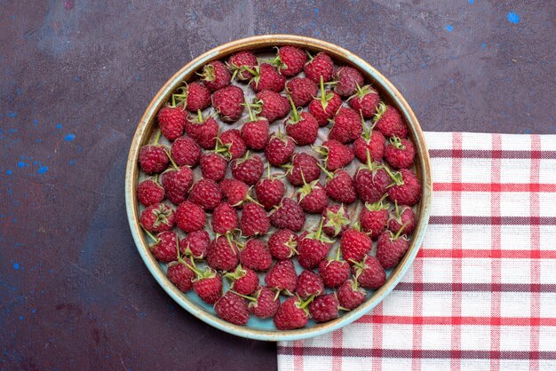 Вид сверху свежей красной малины, спелых ягод внутри круглой миски на темной поверхности, свежие ягоды