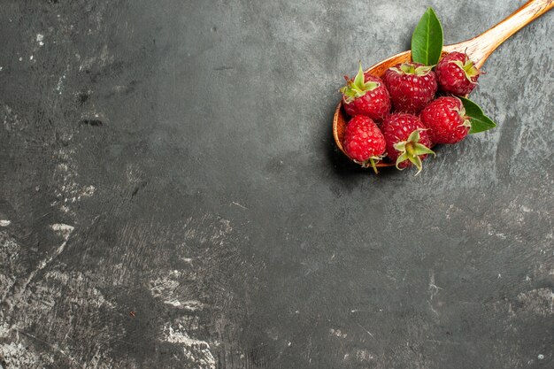 Top view fresh red raspberries on wooden spoon on grey background