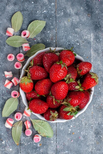 Top view of fresh red strawberries inside plate along with sliced pink candies on grey, fruit berry fresh mellow