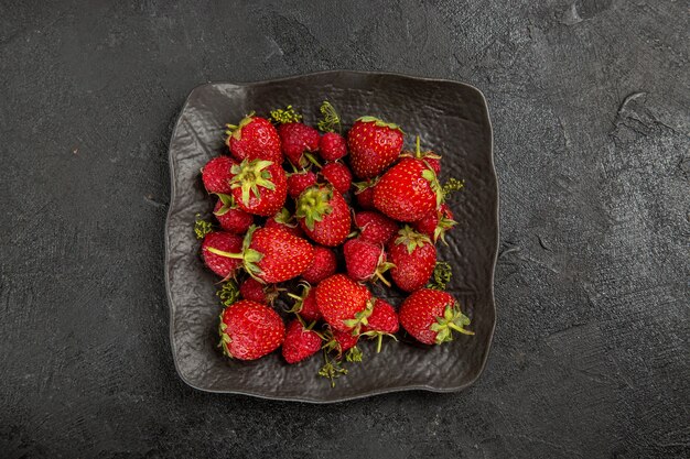 Вид сверху свежей красной клубники внутри тарелки на темных столовых фруктовых ягодах