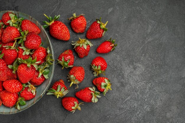 Top view fresh red strawberries inside plate and on grey background