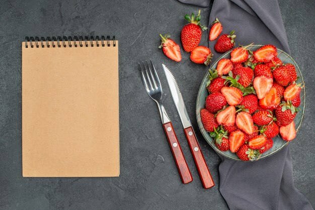 어두운 배경에 메모장이 있는 접시 안에 있는 상단 보기 신선한 빨간 딸기