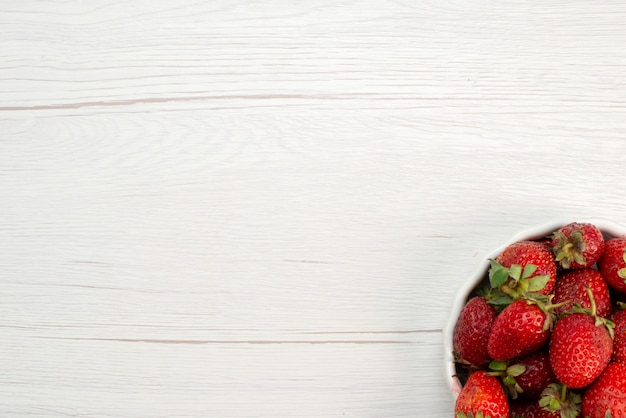 Foto gratuita vista dall'alto di fragole rosse fresche bacche morbide e deliziose all'interno del piatto bianco su luce, bacca di frutta fresca rossa